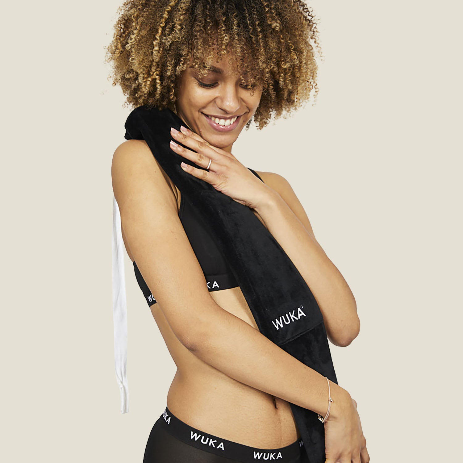 Woman smiling while holding a long black wearable hot water bottle with WUKA logo over her shoulder.