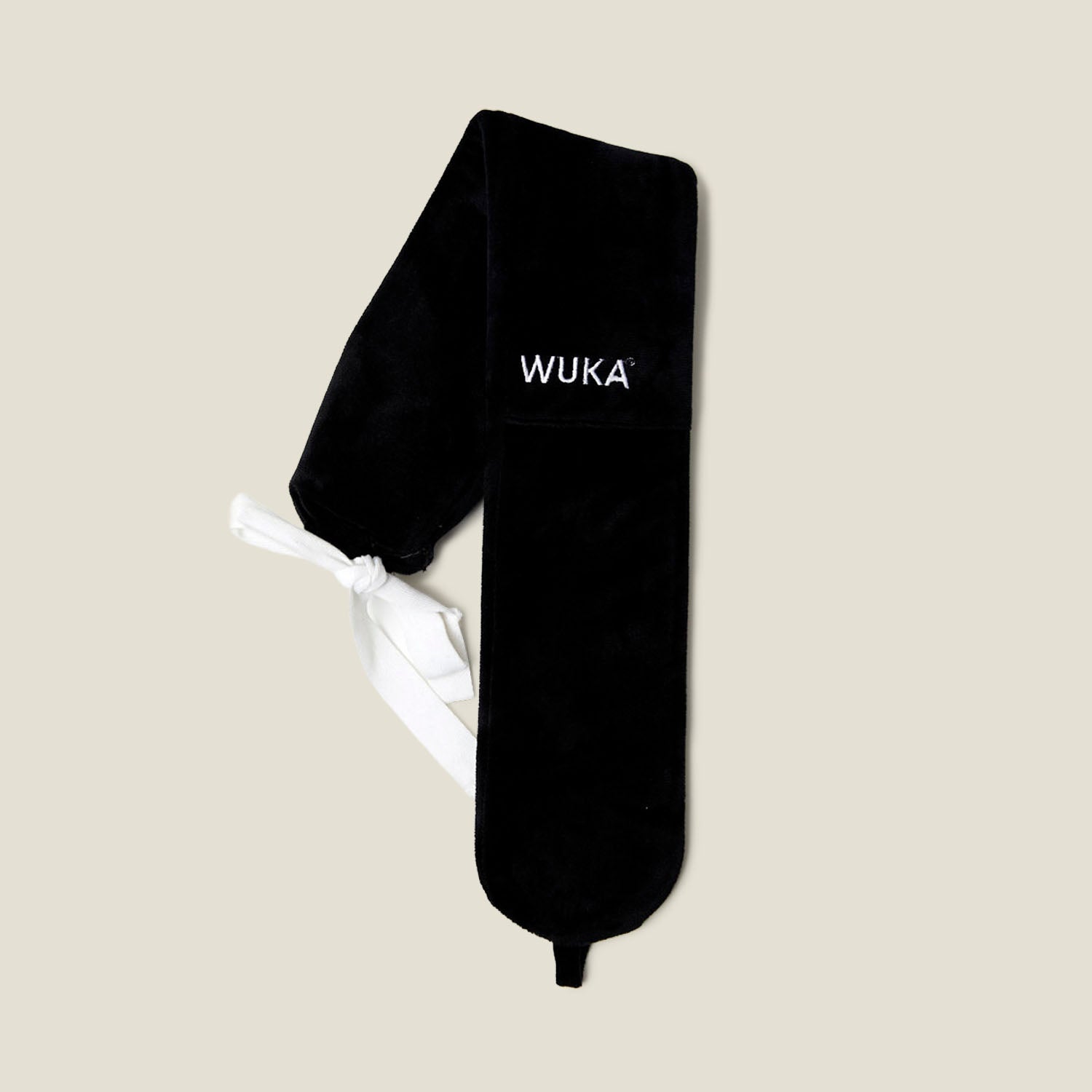 Flat lay of WUKA wearable hot water bottle with long black fleece cover and white tie straps for adjustable fit.